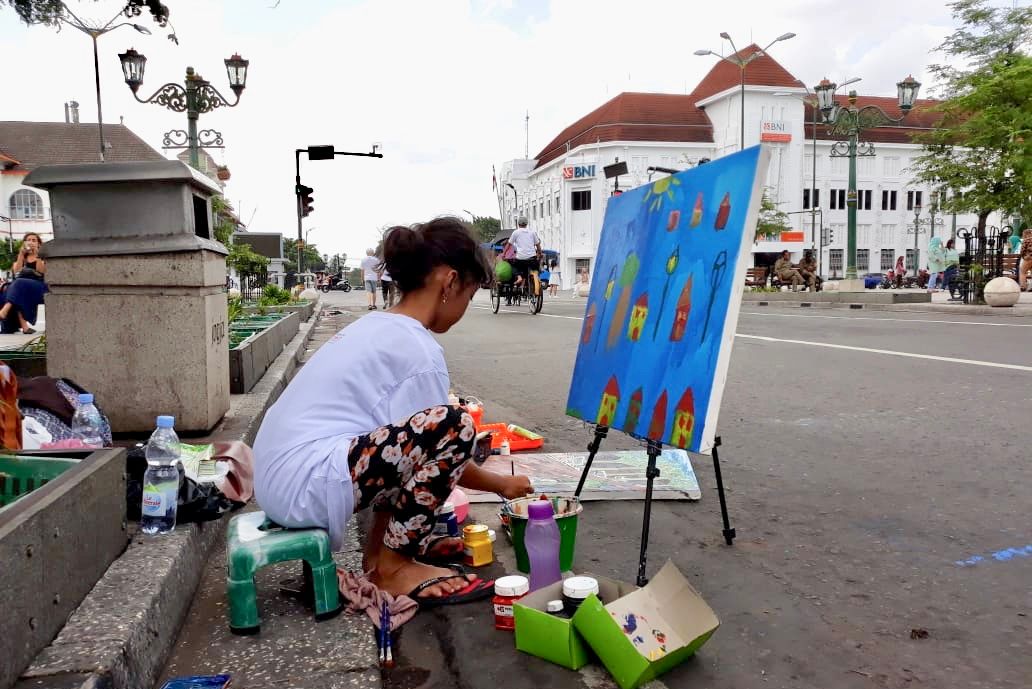 Seorang perupa tengah melukis di Malioboro