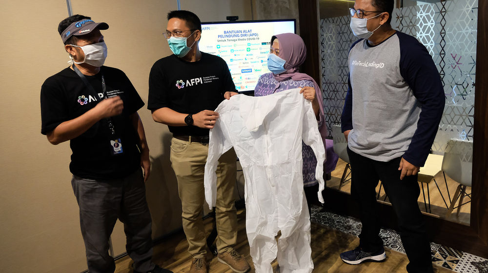 <p>Ketua Harian Asosiasi Fintech Pendanaan Bersama Indonesia (AFPI), Kuseryansyah (Kiri) Bersama Kepala Bidang Humas dan Kelembagaan AFPI, Tumbur Pardede (kedua kiri), Kepala Eksekutif Fintech Pendanaan Multiguna. Dino Martin (Kanan) serta perwakilan Rumah sakit Husada menunjukkan baju pelindung diri saat penyerahan paket bantuan Alat Pelindung Diri (APD) dalam penanganan wabah Covid-19 di Sekretariat AFPI di Jakarta, Kamis (9/4). Foto: Ismail Pohan/TrenAsia</p>