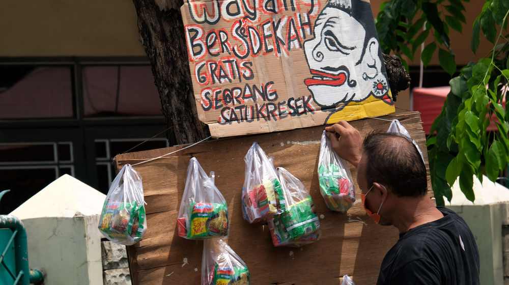 <p>Seniman wayang uwuh Iskandar Hardjodimuljo menggantungkan paket bahan makanan di batang pohon yang akan dibagikan kepada warga yang melintas di Jalan Cawang Baru Utara, Jakarta Timur, Kamis (16/4/2020). Aksi bertajuk “Wayang Bersedekah” ini merupakan inisiatif Iskandar dalam menanggapi kondisi pandemi corona. Bahan makanan yang dibagikan kepada warga di dapat dari hasil penjualan wayang berbahan sampah daur ulang. Dalam sehari rata-rata sebanyak 20 paket makanan dibagikan untuk warga yang kesulitan akibat dampak pandemi COVID-19 saat ini. Foto: Ismail Pohan/TrenAsia</p>
