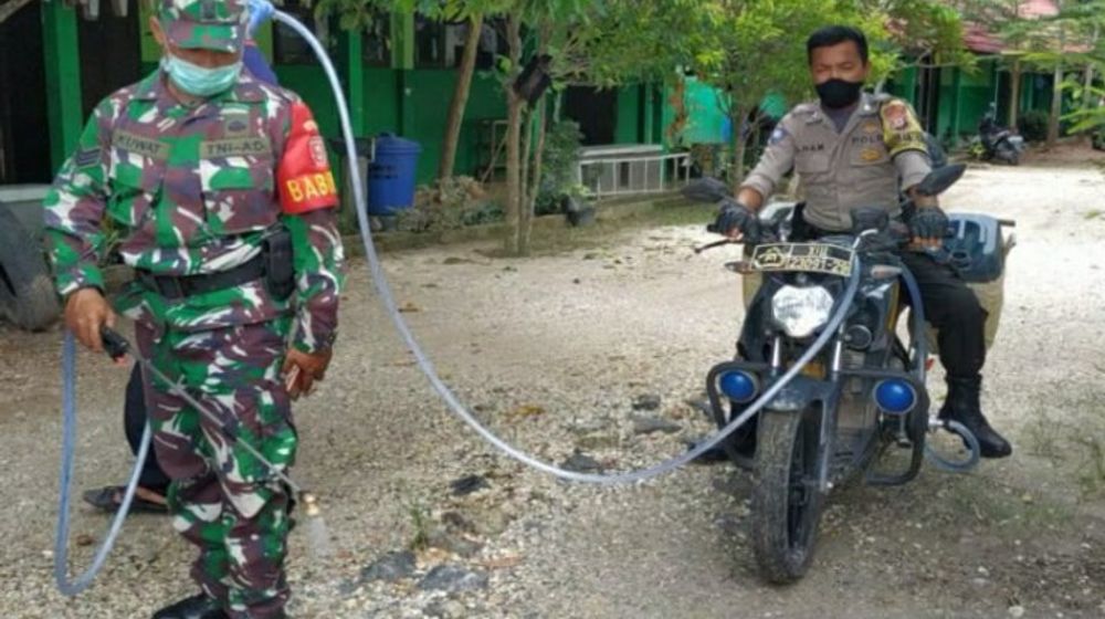<p>Bripka Fakhrin Ilham bersama Babinsa melakukan penyemprotan disinfektan ke lingkungan sekolah menggunakan motor Bhabinkamtibmas yang telah dimodifikasi. /Antara</p>
