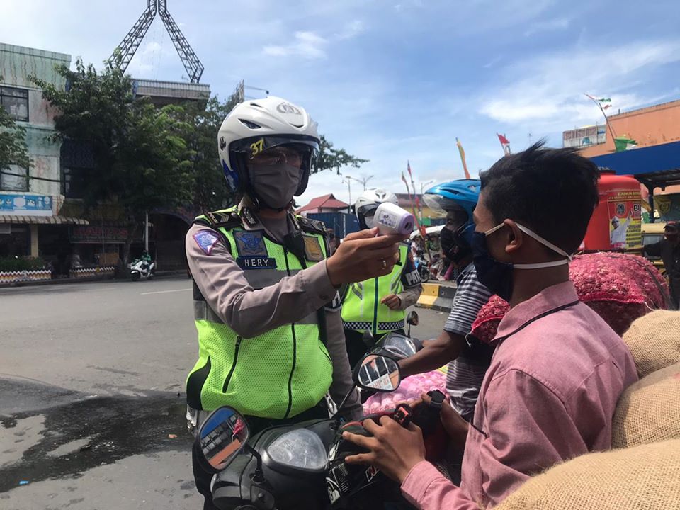 Petugas memeriksa suhu tubuh warga yang akan beraktivitas di pasar tradisional