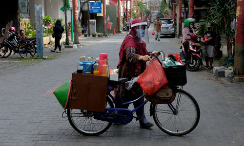 <p>Tidar (46), mendorong sepeda nya berjualan jamu keliling di Pasar Baru, Jakarta Pusat, Kamis 11 Juni 2020. Penjual jamu tradisional keliling ini tampak mematuhi protokol kesehatan pencegahan COVID-19 dengan mengenakan masker, face shield, dan sarung tangan dalam melayani pelanggan setianya di masa PSBB transisi. Foto: Ismail Pohan/TrenAsia</p>
