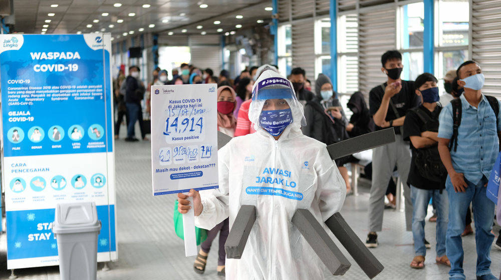 <p>Maskot ‘Manusia Covid’ dari anggota komunitas pecinta Transjakarta mengenakan hazmat dengan membawa poster berisi informasi jumlah kasus positif di Jakarta saat melakukan sosialisasi protokol kesehatan di Halte Transjakarta Harmoni, Jakarta, Rabu, 15 Juli 2020. Sosialisasi tersebut untuk mengingatkan penumpang Transjakarta agar selalu menaati protokol kesehatan saat menggunakan transportasi publik untuk memutus rantai penyebaran COVID-19. Foto: Ismail Pohan/TrenAsia</p>

