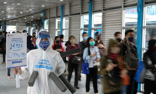 <p>Maskot ‘Manusia Covid’ dari anggota komunitas pecinta Transjakarta mengenakan hazmat dengan membawa poster berisi informasi jumlah kasus positif di Jakarta saat melakukan sosialisasi protokol kesehatan di Halte Transjakarta Harmoni, Jakarta, Rabu, 15 Juli 2020. Sosialisasi tersebut untuk mengingatkan penumpang Transjakarta agar selalu menaati protokol kesehatan saat menggunakan transportasi publik untuk memutus rantai penyebaran COVID-19. Foto: Ismail Pohan/TrenAsia</p>
