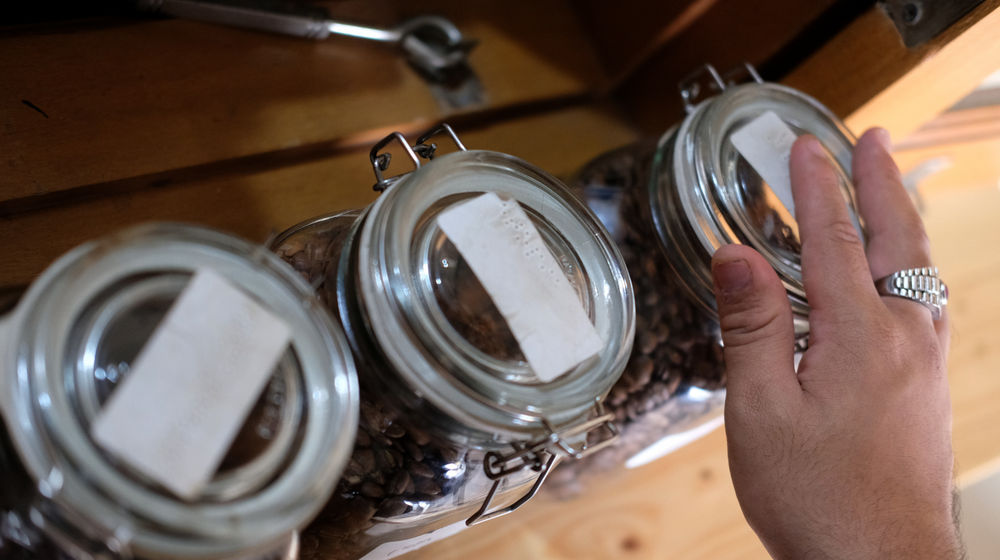 <p>Ahmad Hilmy Almusawa (22) penyandang tuna netra membaca huruf braille saat memilih biji kopi untuk pesanan pelanggan di gerainya “Mata Hati Koffie”, kawasan Pondok Cabe, Tangerang Selatan, Kamis, 23 Juli 2020. Meski dalam situasi pandemi, Hilmy yang sudah mengalami kebutaan sejak umur 12 tahun ini tetap semangat meracik kopi dengan hati di gerai miliknya sendiri tersebut. Omset yang menurun tidak serta merta menurunkan semangatnya untuk tetap menjalankan bisnisnya dengan sepenuh hati melayani setiap penikmat kopi yang datang tak terkecuali pelanggan setianya. Foto: Ismail Pohan/TrenAsia</p>
