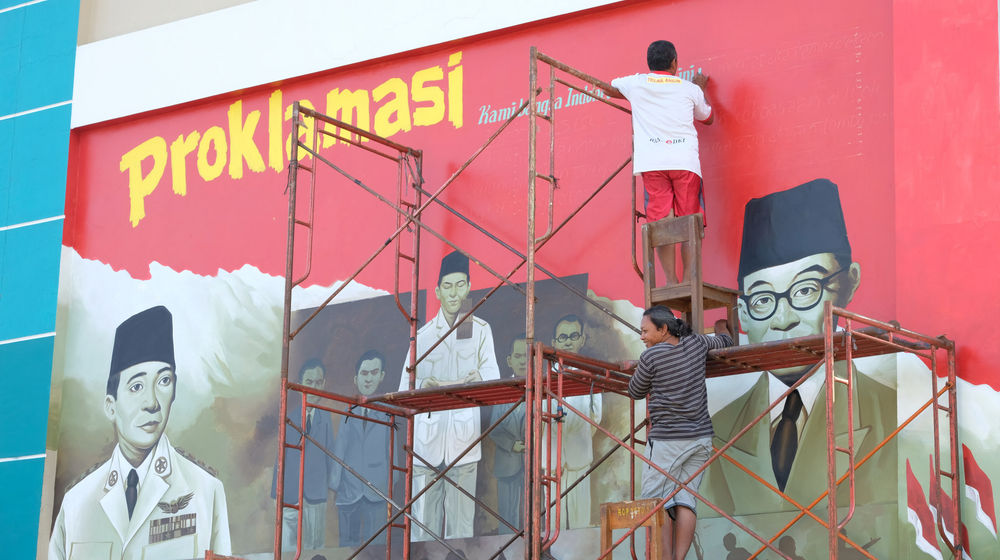 <p>Seniman mengerjakan pembuatan mural bertemakan Proklamasi di Sekolah Dasar Negeri (SDN) Pondok Aren 02, Tangerang Selatan, Banten, Rabu, 22 Juli 2020. Mural tersebut dibuat dalam rangka menyambut  HUT  ke-75 RI tahun ini yang mengusung tema “Indonesia Maju”. Namun karena masih berada dalam situasi pandemi COVID-19, pemerintah menyerukan agar peringatan digelar secara sederhana dengan tetap menerapkan protokol kesehatan kenormalan baru. Foto: Ismail Pohan/TrenAsia</p>
