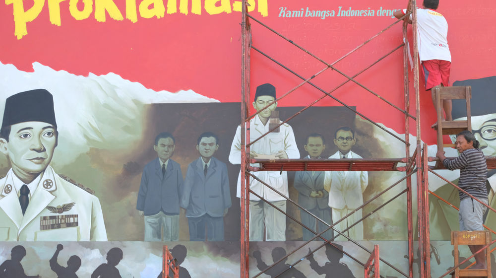 <p>Seniman mengerjakan pembuatan mural bertemakan Proklamasi di Sekolah Dasar Negeri (SDN) Pondok Aren 02, Tangerang Selatan, Banten, Rabu, 22 Juli 2020. Mural tersebut dibuat dalam rangka menyambut HUT ke-75 RI tahun ini yang mengusung tema “Indonesia Maju”. Namun karena masih berada dalam situasi pandemi COVID-19, pemerintah menyerukan agar peringatan digelar secara sederhana dengan tetap menerapkan protokol kesehatan kenormalan baru. Foto: Ismail Pohan/TrenAsia</p>