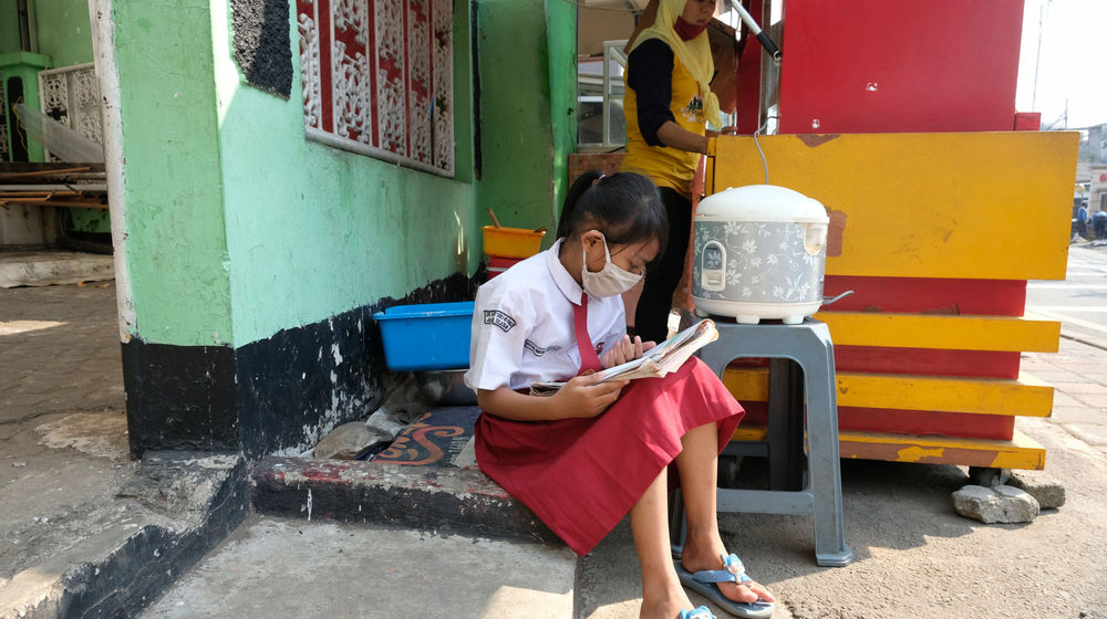 <p>Keysha (8) mengikuti pelajaran secara online di gerai ayam krispy tempat ibunya bekerja, di Jalan Bukit Duri Tanjakan, Gang Langgar, Jakarta Selatan, Selasa, 28 Juli 2020. Anak pertama dari tiga bersaudara pasangan Firman (32) dan Okta (31) tampak tekun mengikuti pelajaran berbasis online di masa kernormalan baru saat ini. Keluarga yang terdampak secara ekonomi akibat ayahnya yang dirumahkan dari pekerjaan, membuat ibunya harus turun tangan dengan bekerja di gerai ayam krispy milik tetangga mereka. Belum lagi sistem sekolah online yang memaksa orang tua Keysha harus menyisihkan penghasilan untuk membeli pulsa Rp 25000 per minggu agar anak mereka dapat terus belajar. Ditengah himpitan ekonomi, Keysha yang bercita-cita menjadi seorang dokter ini terus memupuk semangatnya untuk belajar agar bisa membanggakan keluarga, sembari berdoa agar ayahnya kembali mendapatkan pekerjaan dan badai corona segera berakhir. Foto: Ismail Pohan/TrenAsia</p>