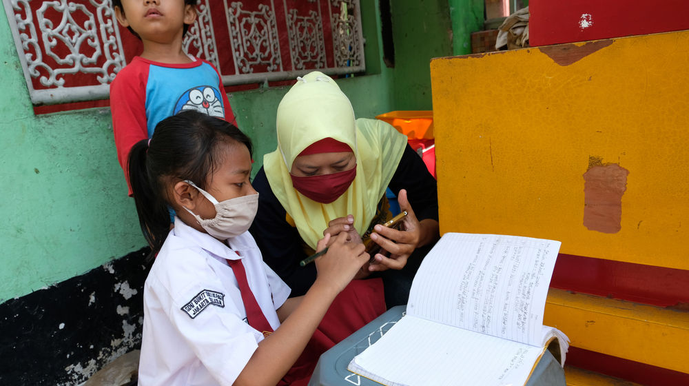 <p>Keysha (8) mengikuti pelajaran secara online didampingi ibundanya di gerai ayam krispy tempat ibunya bekerja, di Jalan Bukit Duri Tanjakan, Gang Langgar, Jakarta Selatan, Selasa, 28 Juli 2020. Anak pertama dari tiga bersaudara pasangan Firman (32) dan Okta (31) tampak tekun mengikuti pelajaran berbasis online di masa kernormalan baru saat ini. Keluarga yang terdampak secara ekonomi akibat  ayahnya yang dirumahkan dari pekerjaan, membuat ibunya harus turun tangan dengan bekerja di gerai ayam krispy milik tetangga mereka. Belum lagi sistem sekolah online yang memaksa orang tua Keysha harus menyisihkan penghasilan untuk membeli pulsa Rp 25000 per minggu agar anak mereka dapat terus belajar. Ditengah himpitan ekonomi, Keysha yang bercita-cita menjadi seorang dokter ini terus memupuk semangatnya untuk belajar agar bisa membanggakan keluarga, sembari berdoa agar ayahnya kembali mendapatkan pekerjaan dan badai corona segera berakhir. Foto: Ismail Pohan/TrenAsia</p>
