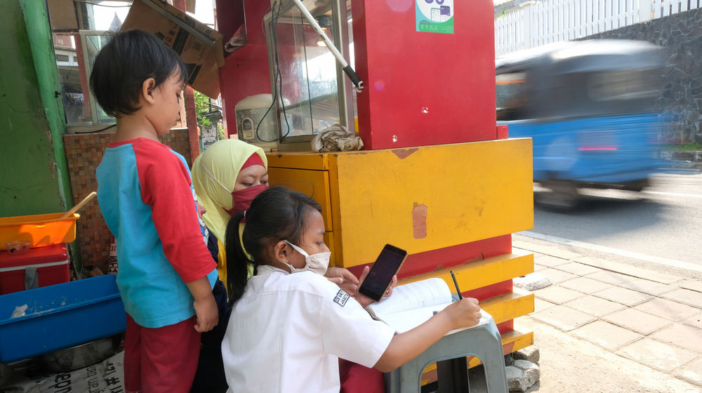 <p>Keysha (8) mengikuti pelajaran secara online di dampingi bunda bersama adiknya di gerai ayam krispy tempat ibunya bekerja, di Jalan Bukit Duri Tanjakan, Gang Langgar, Jakarta Selatan, Selasa, 28 Juli 2020. Anak pertama dari tiga bersaudara pasangan Firman (32) dan Okta (31) tampak tekun mengikuti pelajaran berbasis online di masa kernormalan baru saat ini. Keluarga yang terdampak secara ekonomi akibat  ayahnya yang dirumahkan dari pekerjaan, membuat ibunya harus turun tangan dengan bekerja di gerai ayam krispy milik tetangga mereka. Belum lagi sistem sekolah online yang memaksa orang tua Keysha harus menyisihkan penghasilan untuk membeli pulsa Rp 25000 per minggu agar anak mereka dapat terus belajar. Ditengah himpitan ekonomi, Keysha yang bercita-cita menjadi seorang dokter ini terus memupuk semangatnya untuk belajar agar bisa membanggakan keluarga, sembari berdoa agar ayahnya kembali mendapatkan pekerjaan dan badai corona segera berakhir. Foto: Ismail Pohan/TrenAsia</p>
