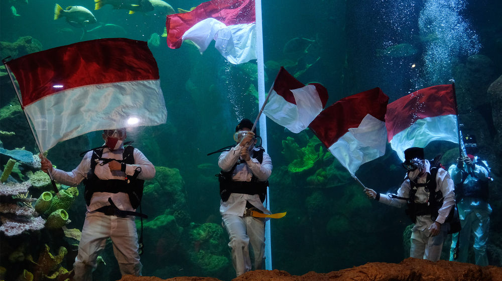 <p>Sejumlah penyelam mengibarkan Bendera Merah Putih saat upacara pengibaran Bendera Peringatan HUT ke-75 RI di Akuarium Utama Sea Word, Ancol, Jakarta, Senin, 17 Agustus 2020. Pengibaran Bendera Merah Putih dan Pembacaan Teks Proklamasi oleh empat orang penyelam profesional Sea Word Ancol tersebut berlangsung hikmat untuk memperingati Hari Kemerdekaan RI. Foto: Ismail Pohan/TrenAsia</p>
