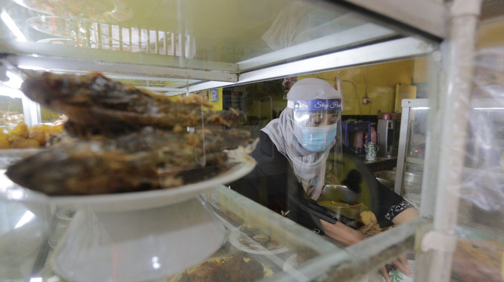 <p>Penjual menggunakan masker dan faceshield saat melayani pelanggan di Warung Tegal (Warteg) Ellya, Cilandak Timur, Jakarta Selatan, Rabu, 5 Agustus 2020. Pemilik warteg mengaku tetap konsisten menerapkan protokol kesehatan pencegahan penyebaran Covid-19 sejak dimulainya masa PSBB transisi hingga saat ini, untuk memastikan keamanan pelanggan yang datang dengan mewajibkan penggunaan masker, menyediakan area cuci tangan, dan pembatasan jarak fisik di area warung tersebut. Foto: Ismail Pohan/TrenAsia</p>