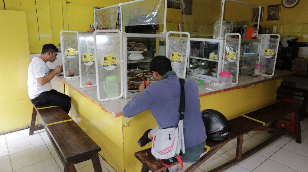 <p>Pelanggan menyantap makanan dengan suasana pembatasan jarak fisik di Warung Tegal (Warteg) Ellya, Cilandak Timur, Jakarta Selatan, Rabu, 5 Agustus 2020. Pemilik warteg mengaku tetap konsisten menerapkan protokol kesehatan pencegahan penyebaran Covid-19 sejak dimulainya masa PSBB transisi hingga saat ini, untuk memastikan keamanan pelanggan yang datang dengan mewajibkan penggunaan masker, menyediakan area cuci tangan, dan pembatasan jarak fisik di area warung tersebut. Foto: Ismail Pohan/TrenAsia</p>
