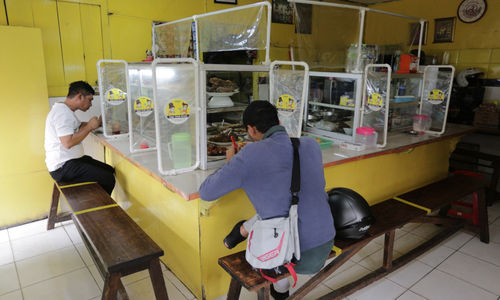 <p>Pelanggan menyantap makanan dengan suasana pembatasan jarak fisik di Warung Tegal (Warteg) Ellya, Cilandak Timur, Jakarta Selatan, Rabu, 5 Agustus 2020. Pemilik warteg mengaku tetap konsisten menerapkan protokol kesehatan pencegahan penyebaran Covid-19 sejak dimulainya masa PSBB transisi hingga saat ini, untuk memastikan keamanan pelanggan yang datang dengan mewajibkan penggunaan masker, menyediakan area cuci tangan, dan pembatasan jarak fisik di area warung tersebut. Foto: Ismail Pohan/TrenAsia</p>