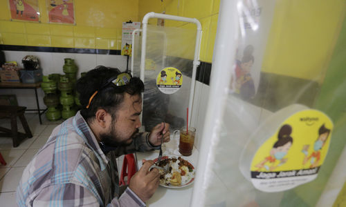 <p>Pelanggan menyantap makanan dengan suasana pembatasan jarak fisik di Warung Tegal (Warteg) Ellya, Cilandak Timur, Jakarta Selatan, Rabu, 5 Agustus 2020. Pemilik warteg mengaku tetap konsisten menerapkan protokol kesehatan pencegahan penyebaran Covid-19 sejak dimulainya masa PSBB transisi hingga saat ini, untuk memastikan keamanan pelanggan yang datang dengan mewajibkan penggunaan masker, menyediakan area cuci tangan, dan pembatasan jarak fisik di area warung tersebut. Foto: Ismail Pohan/TrenAsia</p>
