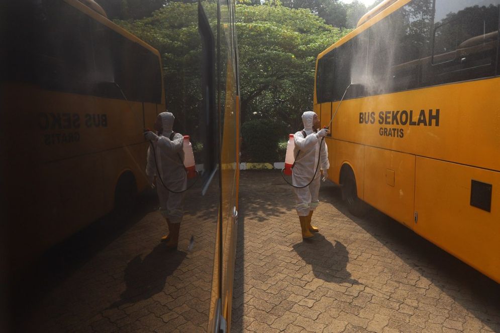 Petugas tengah menyemprotan disinfektan kepada bus sekolah sebelum melakukan penjemputan pasien Covid-19/Foto: Ismail Pohan/TrenAsia