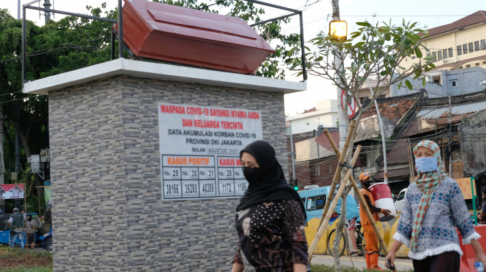 <p>Warga melintas di dekat tugu peti jenazah dan data yang menunjukkan jumlah kasus  COVID-19 di Taman Tongtek, Jatinegara, Jakarta, Selasa, 1 September 2020. Pemprov DKI Jakarta memasang replika peti mati dan papan himbauan waspada COVID-19 di sejumlah lokasi  DKI Jakarta yang masih menjadi wilayah tertinggi penyebaran kasus, dari 2.775 tambahan kasus hari ini, DKI Jakarta menjadi provinsi terbanyak, yakni 901 kasus. Foto: Ismail Pohan/TrenAsia</p>
