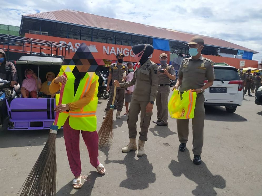 Seorang warga tengah membersihkan jalan di Pasar Nanggalo sebagai sanksi karena tidak menggunakan masker/Foto: Humas Satpol PP Padang