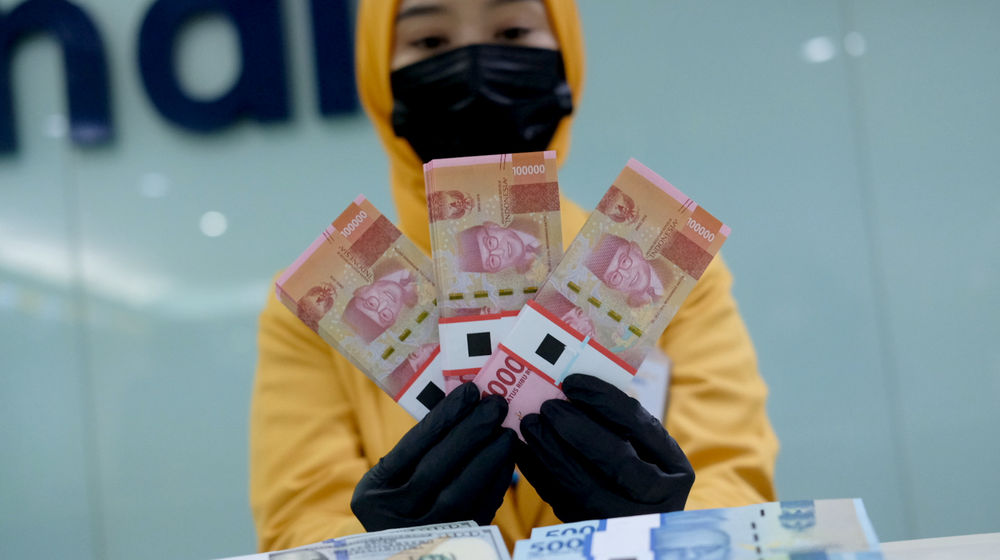 <p>Karyawati menunjukkan mata uang rupiah dan dolar di kantor cabang Bank Mandiri, Jakarta, Senin, 22 Maret 2021. Foto: Ismail Pohan/TrenAsia</p>