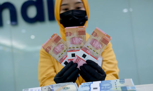 <p>Karyawati menunjukkan mata uang rupiah dan dolar di kantor cabang Bank Mandiri, Jakarta, Senin, 22 Maret 2021. Foto: Ismail Pohan/TrenAsia</p>
