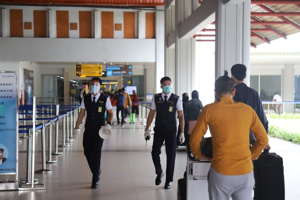 Situasi Bandara I Gusti Ngurah Rai. Tampak dua orang petugas yang senantiasa mensosialisasikan penerapan prokes pada penumpang pesawat udara.