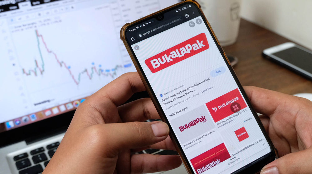 Warga mengakses logo Bukalapak melalui gawai dengan latar grafik pergerakan IHSG di Jakarta, Kamis, 24 Juni 2021.
