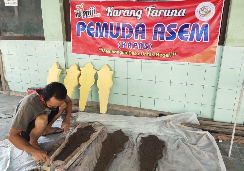 Seorang anggota Karang Taruna Pemuda Asem, Desa Tanjungsepreh, Kecamatan Maospati, Kabupaten Magetan, Jawa Timur tengah mencetak batu nisan, beberapa waktu lalu.