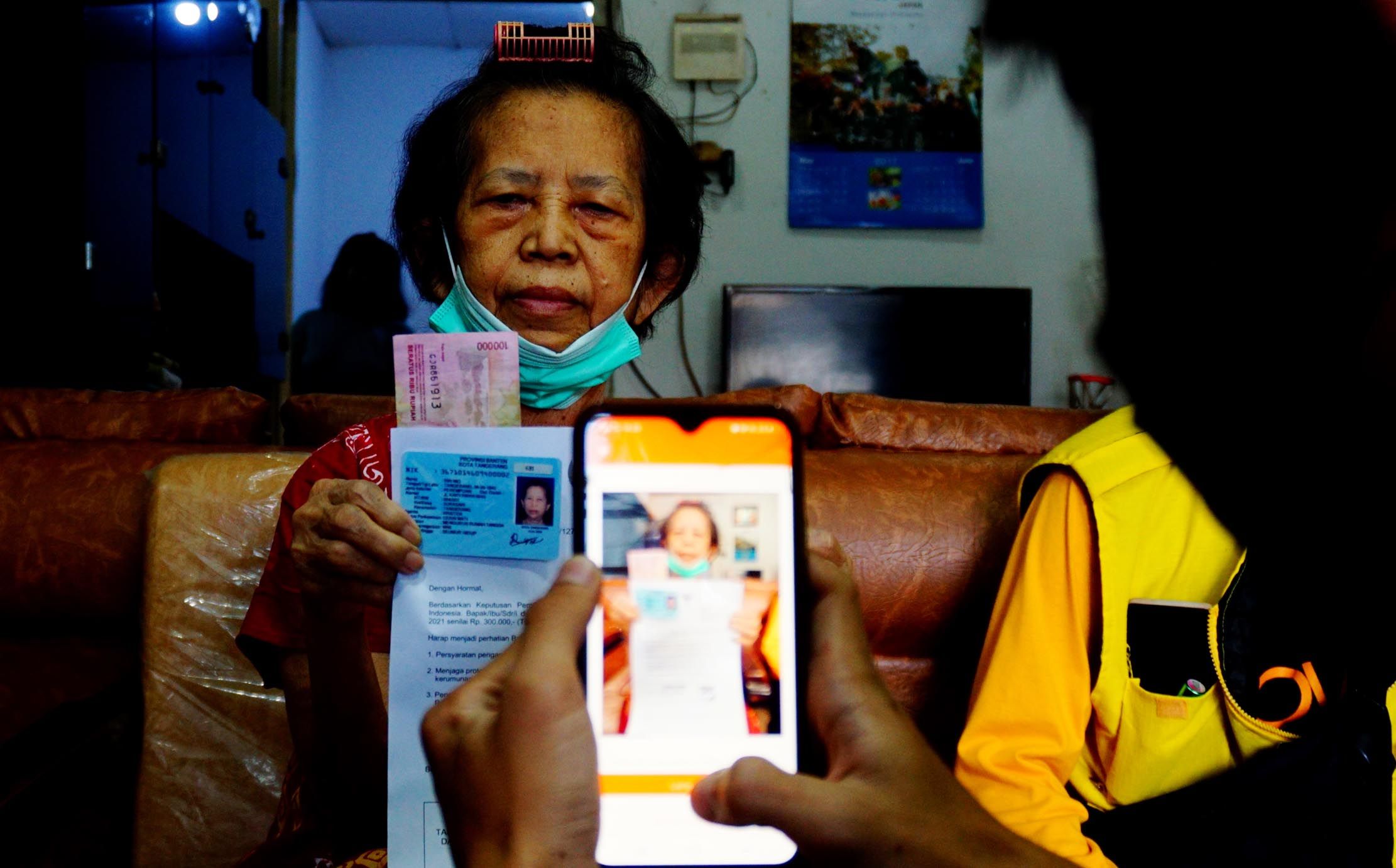 Petugas memfoto data dan KTP warga penerima bantuan saat penyaluran bantuan sosial tunai (BST) yang disalurkan melalui PT Pos Indonesia dengan sistem door to door di wilayah Tangerang, Sabtu 24 Juli 2021. Foto: Panji Asmoro/TrenAsia                               