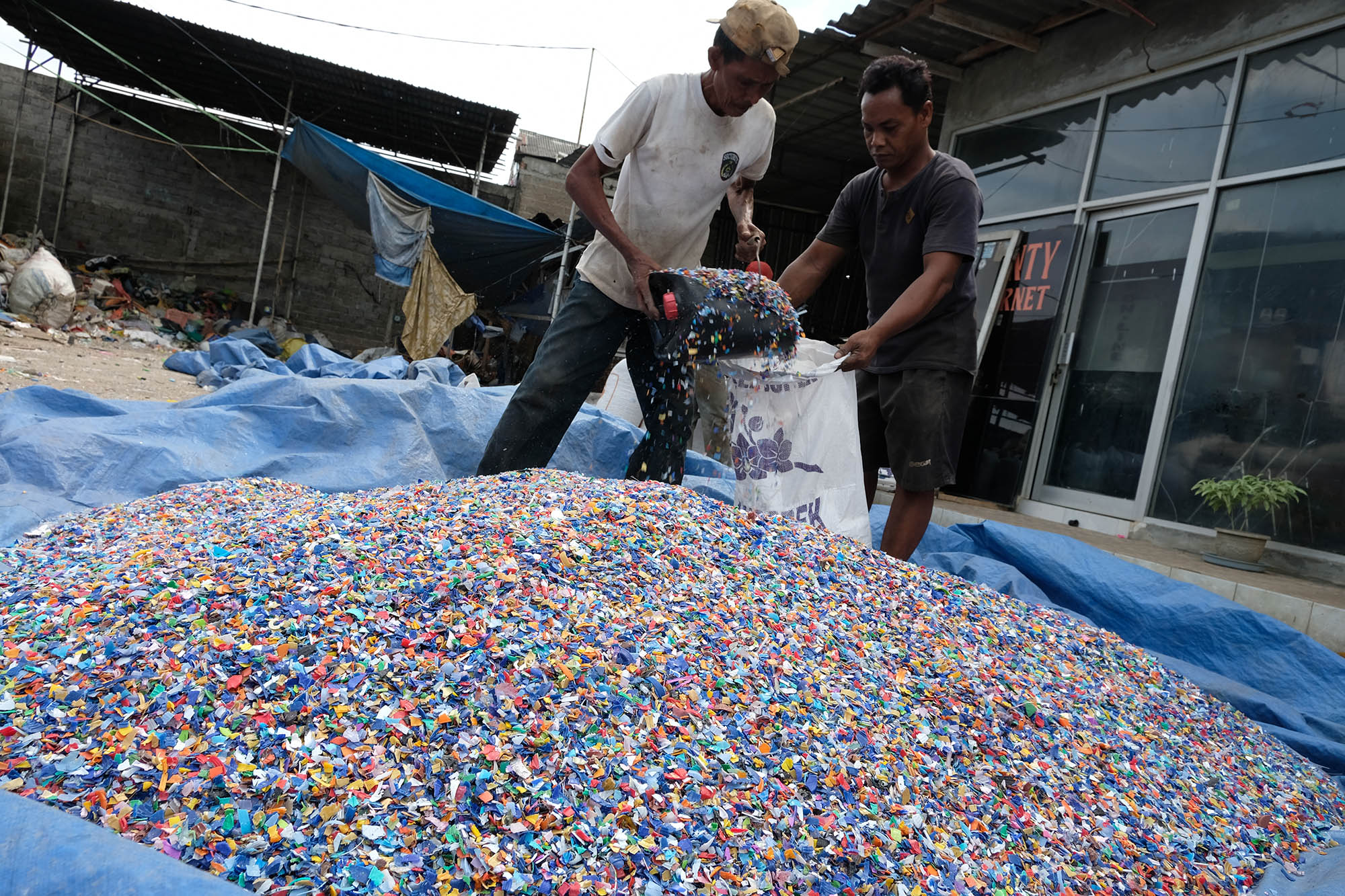 Pekerja memasukkan leburan sampah plastik yang sudah dijemur kedalam karung untuk kemudian ditimbang di gudang pengolahan sampah plastik kawasan Bekasi, Selasa, 14 September 2021. Foto: Ismail Pohan/TrenAsia