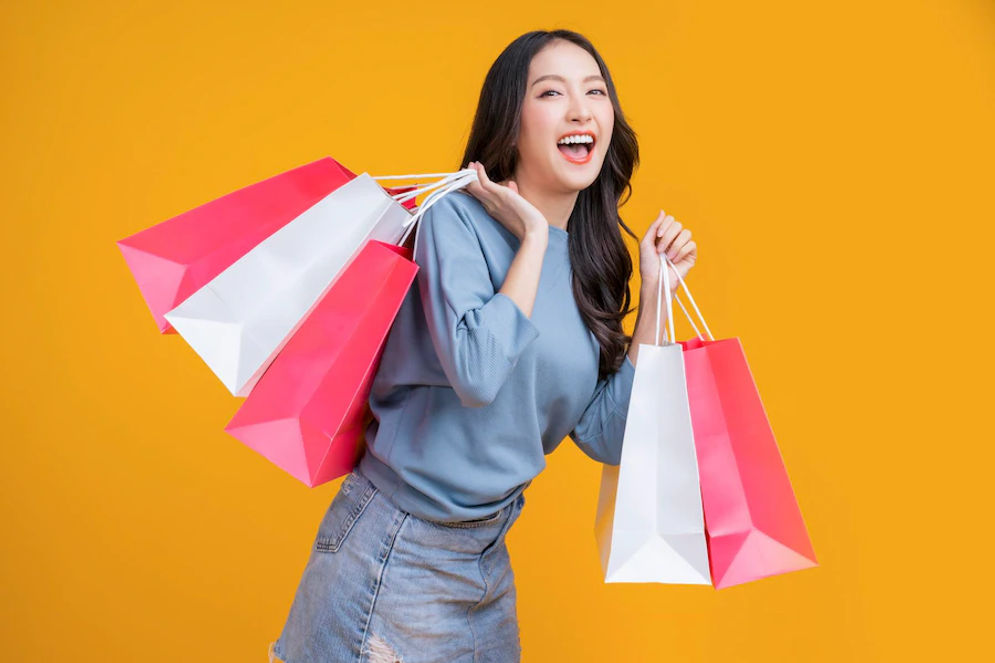 asian-happy-female-woman-girl-holds-colourful-shopping-packages-standing-yellow-background-studio-shot-close-up-portrait-young-beautiful-attractive-girl-smiling-looking-camera-with-bags_609648-3029.webp