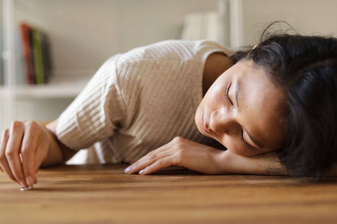 Ron Lach 
A Sad Woman Looking at the Ring she is Holding while Lying Her Face on a Wooden Surface
