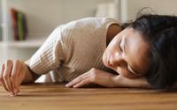 Ron Lach 
A Sad Woman Looking at the Ring she is Holding while Lying Her Face on a Wooden Surface
