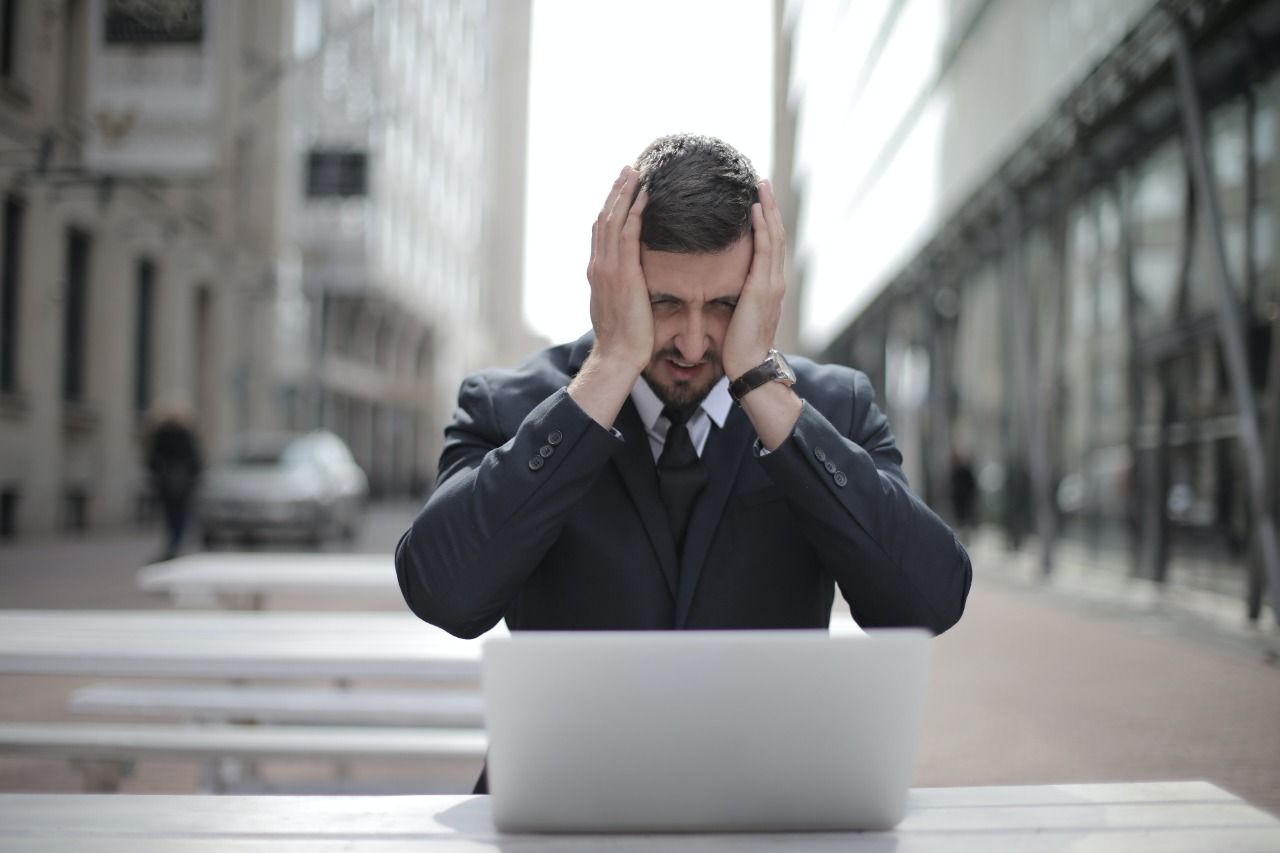 Man in Black Suit Covering His Face With Two Hands
