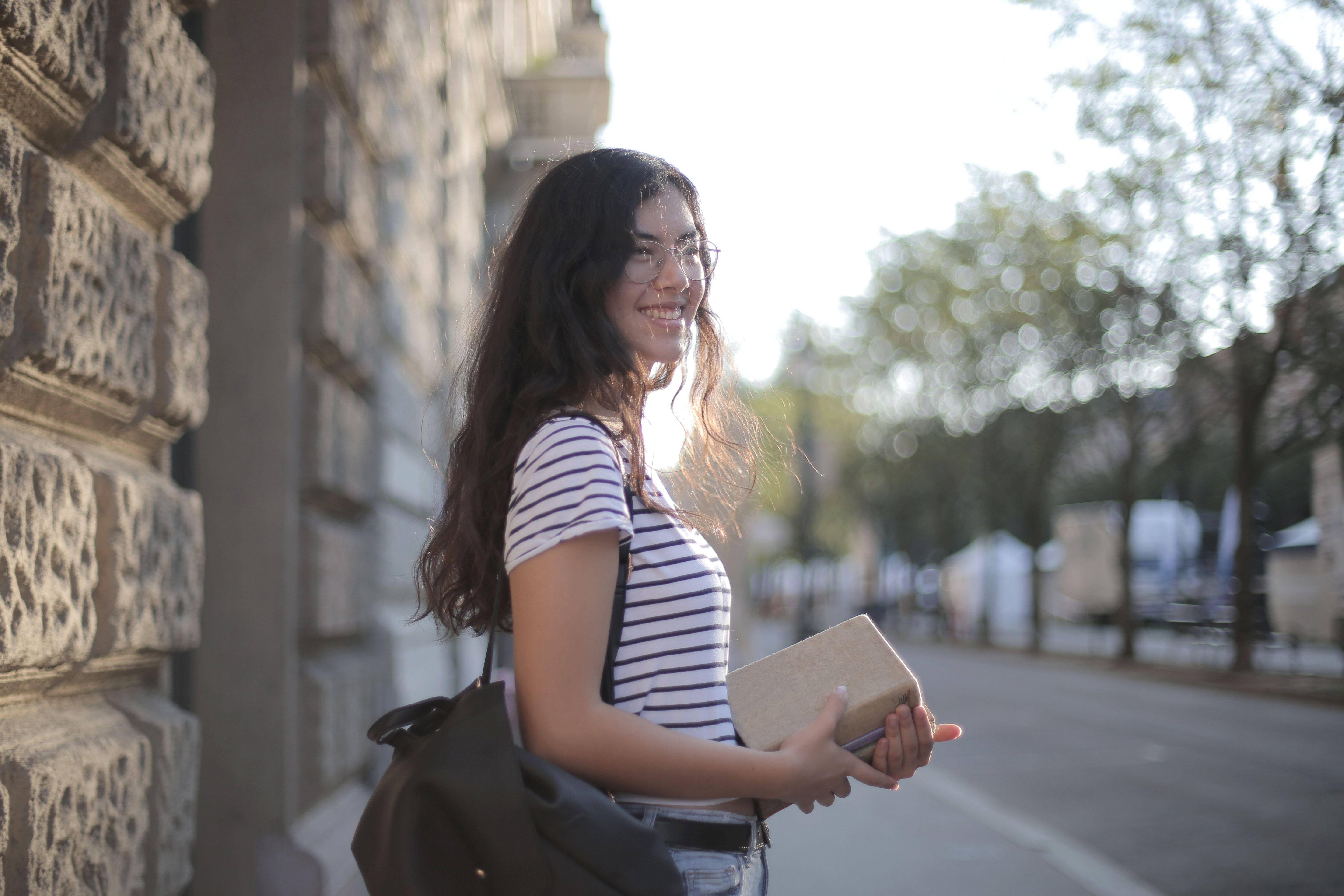 Photo by Andrea Piacquadio: https://www.pexels.com/photo/optimistic-ethnic-woman-with-stack-of-books-in-city-3808181/