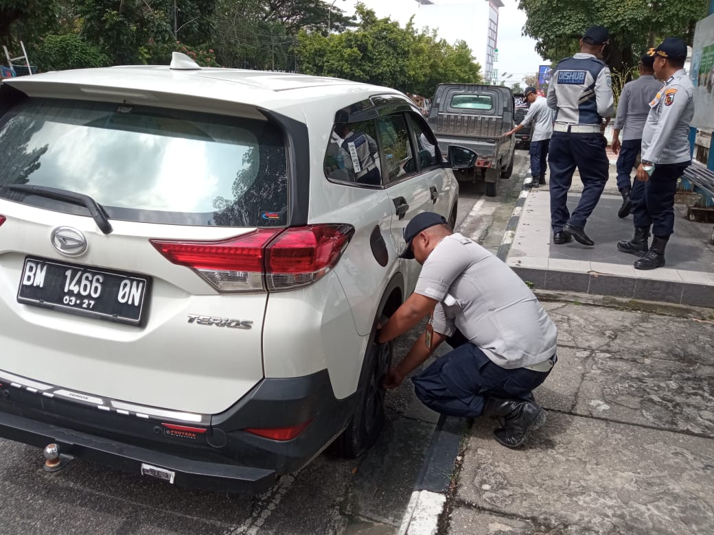 Petugas menggembok mobil yang parkir sembarangan di badan jalan.