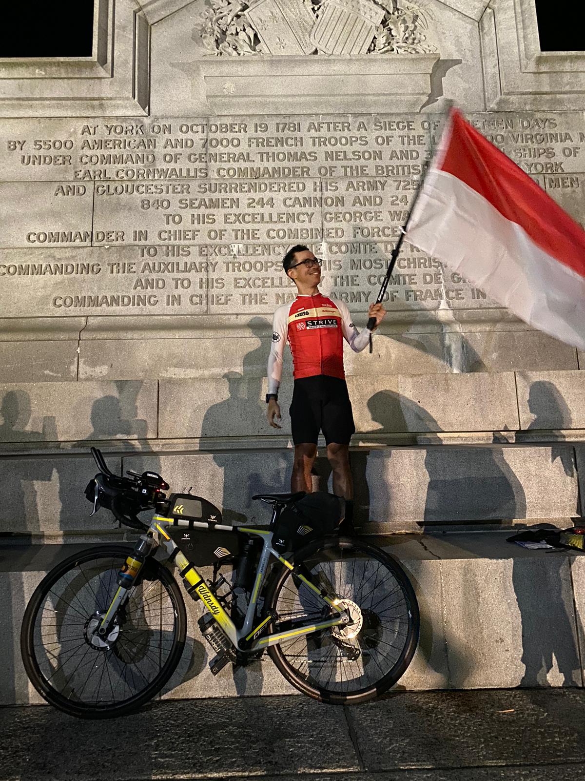 Dzaki Wardana mengibarkan bendera merah putih tepat di titik finis Trans Am Bike Race (TABR) di Yorktown, Virginia.