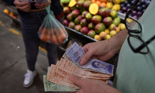 Seorang Pelanggan Menghitung Uang Kertas Bolivar Venezuela di Sebuah Kios di Pasar Kota di Caracas
