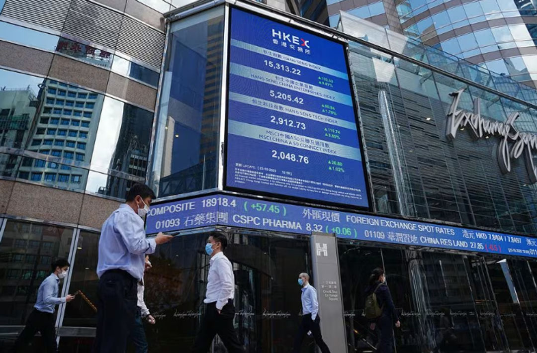 Orang-Orang Berjalan Melewati Layar yang Menampilkan Indeks Saham Hang Seng di Central district, Hong Kong (Reuters/Lam Yik)