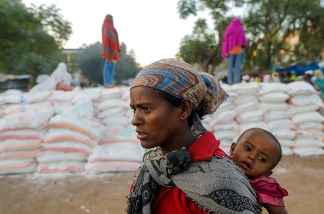 Seorang Wanita Menggendong Seorang Bayi Saat Mengantri untuk Mendapatkan Makanan (Reuters/Baz Ratner)