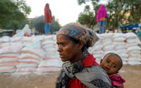 Seorang Wanita Menggendong Seorang Bayi Saat Mengantri untuk Mendapatkan Makanan (Reuters/Baz Ratner)