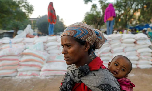 Seorang Wanita Menggendong Seorang Bayi Saat Mengantri untuk Mendapatkan Makanan (Reuters/Baz Ratner)