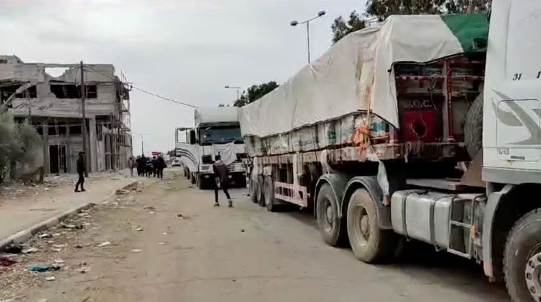 Orang-Orang Berjalan di Samping Truk dengan Bantuan Kemanusiaan yang Dikirimkan oleh Masyarakat Bulan Sabit Merah Palestina, menuju Gaza Utara (Reuters)