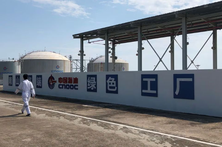 Seorang Pekerja Berjalan Melewati Logo Perusahaan Minyak Lepas Pantai Nasional China (CNOOC) di Terminal Gas Alam Cair (LNG) Nanshan di provinsi Hainan, China (Reutrs/Muyu Xu)