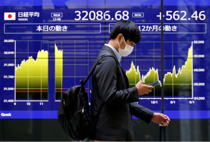 Seorang Pria Berjalan Melewati Monitor Listrik yang Menampilkan Rata-Rata Saham Nikkei Jepang dan Pergerakan Terkini (Reuters/Issei Kato)