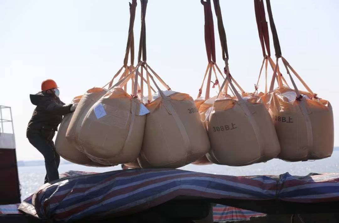 Seorang Pekerja yang Memakai Masker, Mengangkut Pupuk untuk Diekspor di Sebuah Pelabuhan di Nantong, Provinsi Jiangsu, China (Reuters/China Daily)