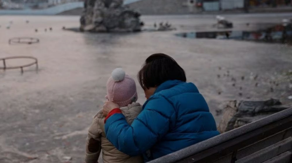 Seorang wanita dan seorang anak duduk di sebuah taman di Beijing