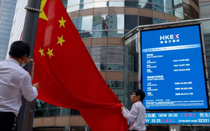 Staf menurunkan bendera nasional China di depan layar yang menampilkan indeks dan harga saham di luar Exchange Square, di Hong Kong, China (Reuters/Tyrone Siu)