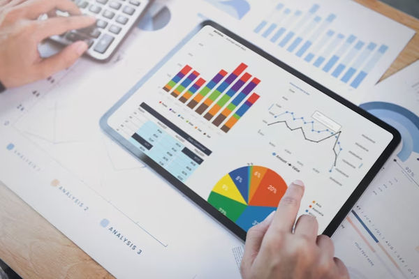 Foto seorang pebisnis menggunakan tablet untuk menganalisis grafik statistik strategi keuangan perusahaan.