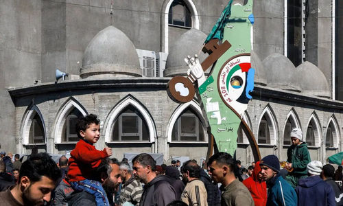 Orang-orang berjalan melewati papan tanda yang menggambarkan peta bersejarah Palestina