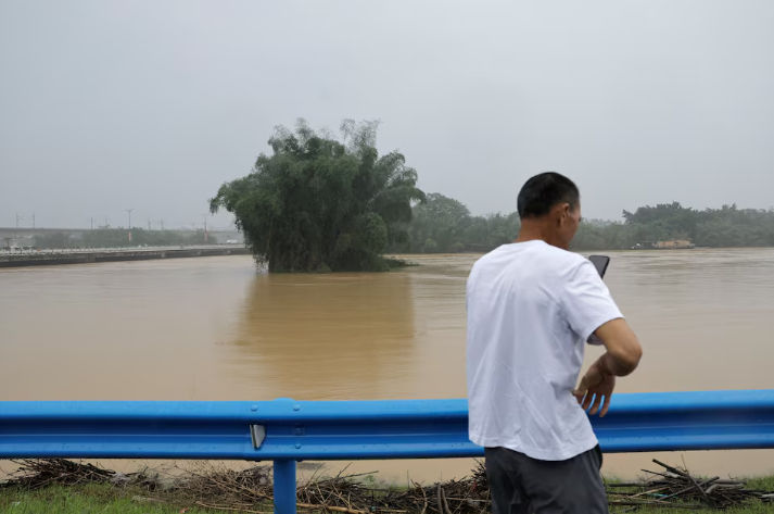 Seorang warga menggunakan ponselnya saat dia berdiri di dekat sungai yang banjir setelah hujan lebat di Qingyuan, provinsi Guangdong, China 22 April 2024. (Reuters/Tingshu Wang)